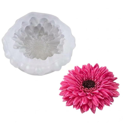 A white silicone mold with a flower-shaped cavity shown next to a real pink daisy flower on a plain white background.