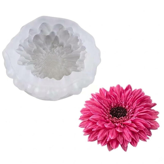 A white silicone mold with a flower-shaped cavity shown next to a real pink daisy flower on a plain white background.