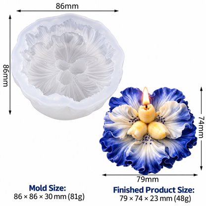 A white floral candle mold shown next to a finished blue-and-white flower candle with a small lit wick. Measurement labels indicate mold size 86 x 86 mm and finished product size 79 x 74 mm on a plain white background.