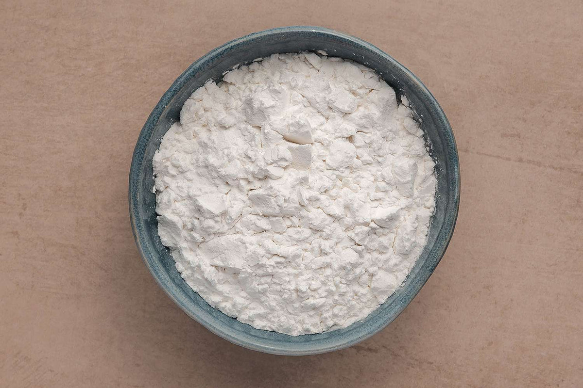 A bowl of fine white arrowroot powder on a plain background.
