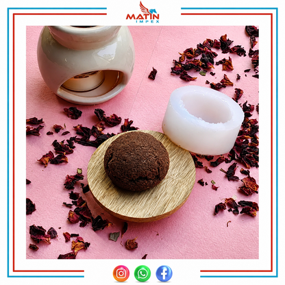 A white silicone wax melt mold shown next to a dark brown wax melt on a small wooden dish, with a ceramic warmer in the background on a pink surface scattered with dried red flower petals. The brand logo 'MATIN IMPEX' is visible at the top.