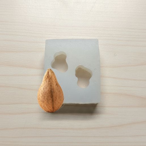 Coconut next to a concrete mold with a teardrop shape on a light wooden surface.