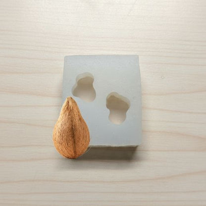 Coconut next to a concrete mold with a teardrop shape on a light wooden surface.