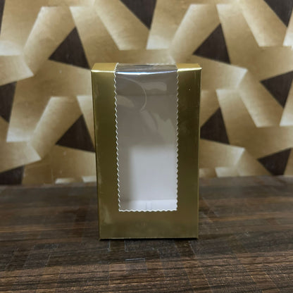Gold gift box with a white window on a wooden surface with a geometric patterned background