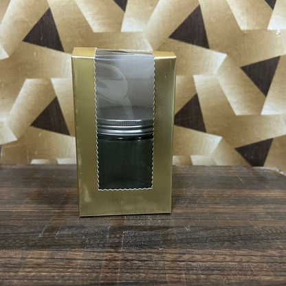 Gold gift box with a black container on a wooden surface with a geometric patterned wall in the background.