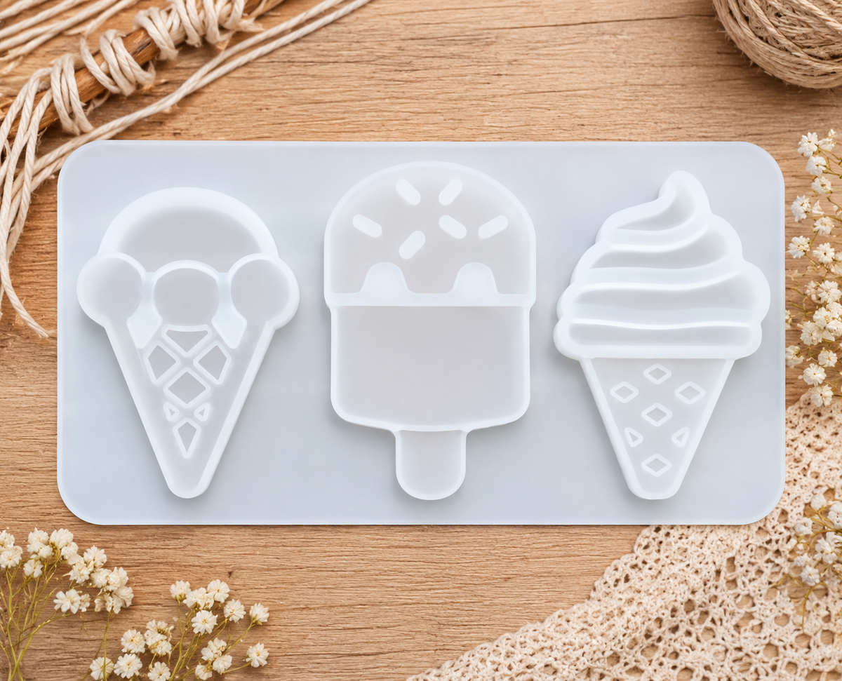A silicone mold tray with three ice cream and popsicle shapes, shown on a wooden surface with decorative dried flowers and twine.