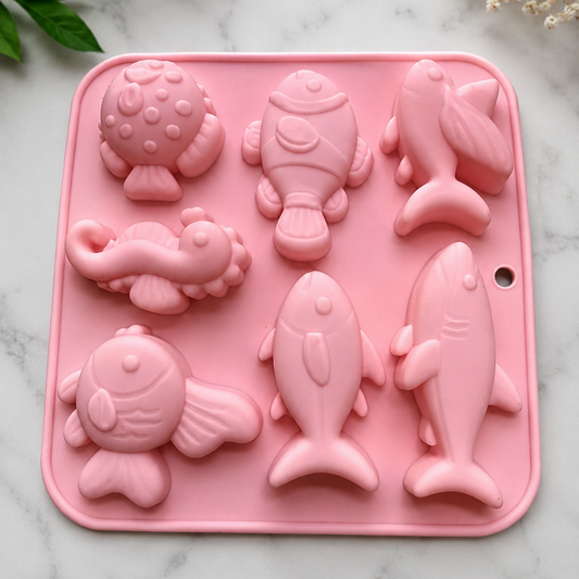 Pink silicone mold with various sea animal shapes on a marble surface.