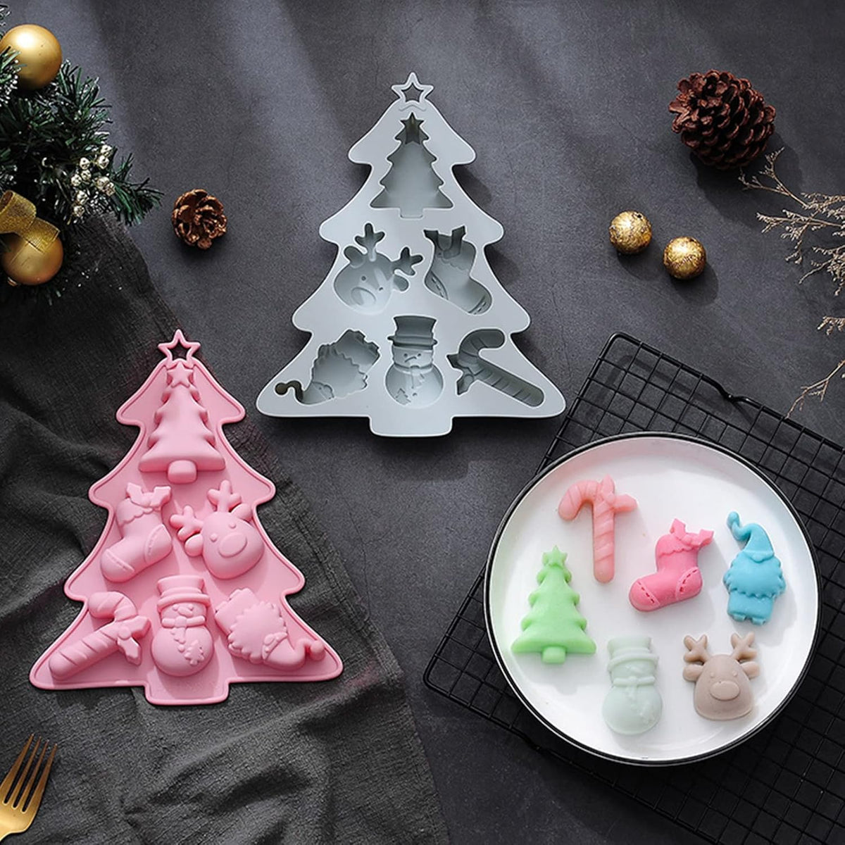 Christmas-themed silicone molds on a dark surface with a plate of shaped candies.