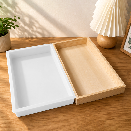 Two wooden trays, one white and one natural wood, on a wooden surface with a plant and lamp in the background.