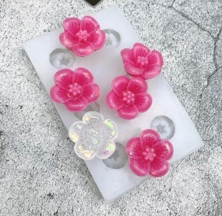 Flower-shaped pink and clear resin molds on a white rectangular base.
